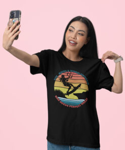 Waves & Windblown Hair – Epic Kite Surfing T-Shirt featuring a bold silhouette of a female kitesurfer soaring over a scenic sunset landscape with a retro-style striped background. The design includes the phrases "KITE, WAVES & WINDBLOWN HAIR" in blue and "WHO NEEDS PERFECT NAILS?" in red, adding a fun, adventurous touch.