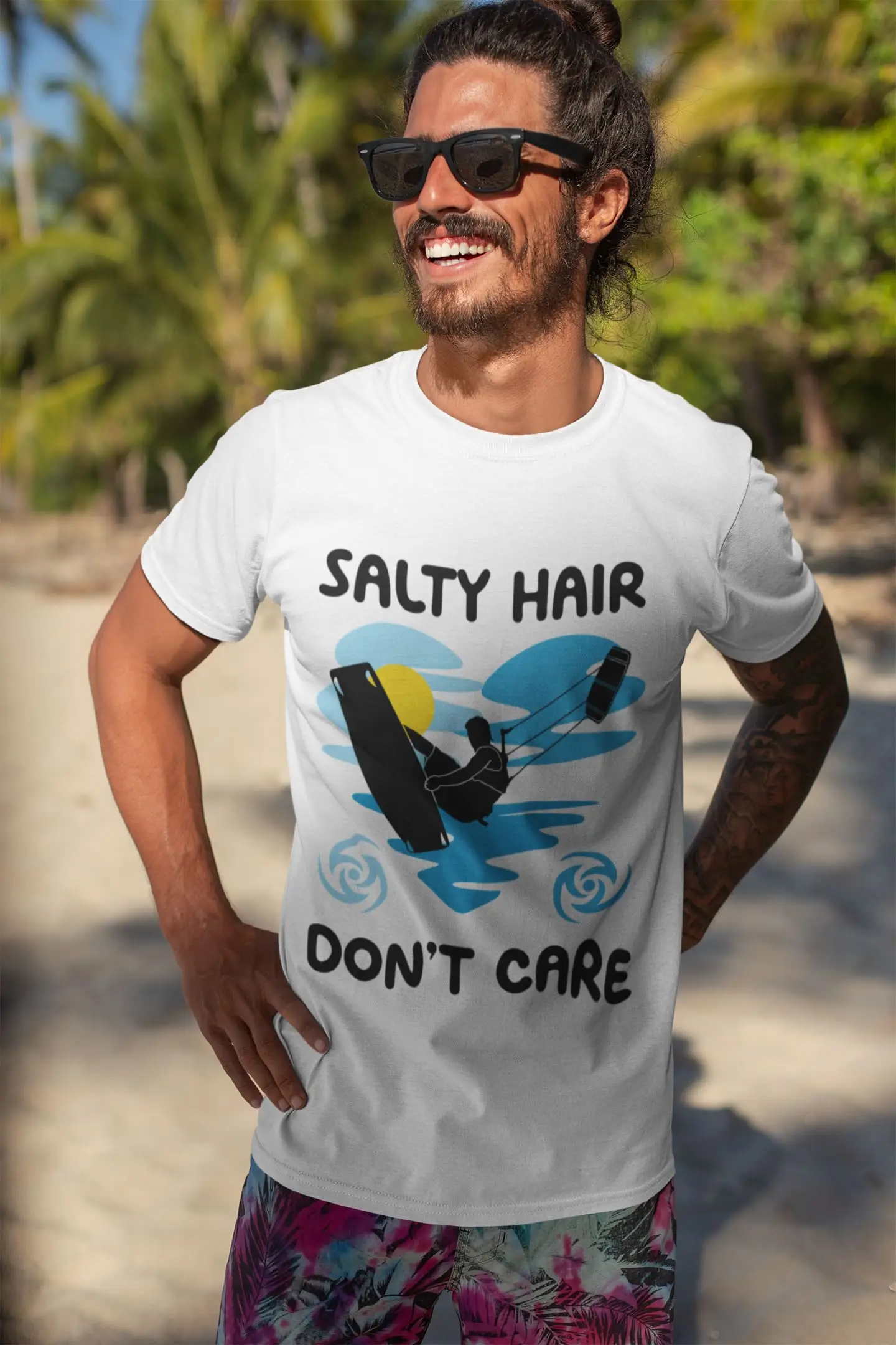 Man on a tropical beach wearing a white "Salty Hair Don’t Care" kitesurfing t-shirt from the surfing collection