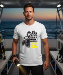A young man standing on the deck of a dive boat at sunset holding a flashlight, wearing a white premium **night diving shirt** with a split scuba diver graphic and bold safety yellow typography