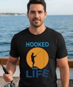 Man standing on a boat deck wearing a black premium fisherman tee with an orange sunset graphic print