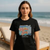 Woman standing on a sunny beach wearing a black premium beach graphic tee with a retro vitamin sea supplement print