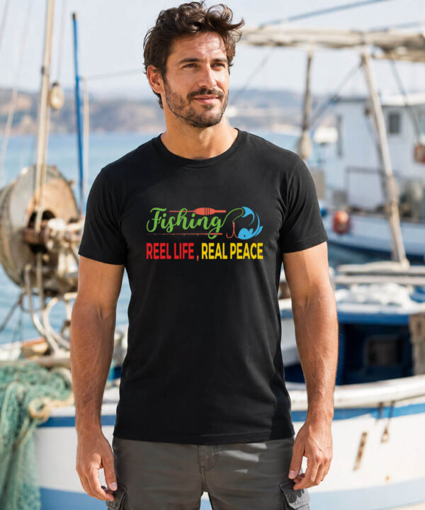 Man wearing black Reel Life Fishing Shirt with reel and lure graphic at marina dock, Seasportees fishing tee