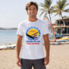 Man wearing white windsurfing t-shirt with sunburst wind-sport graphic and Harness the Wind text on beach
