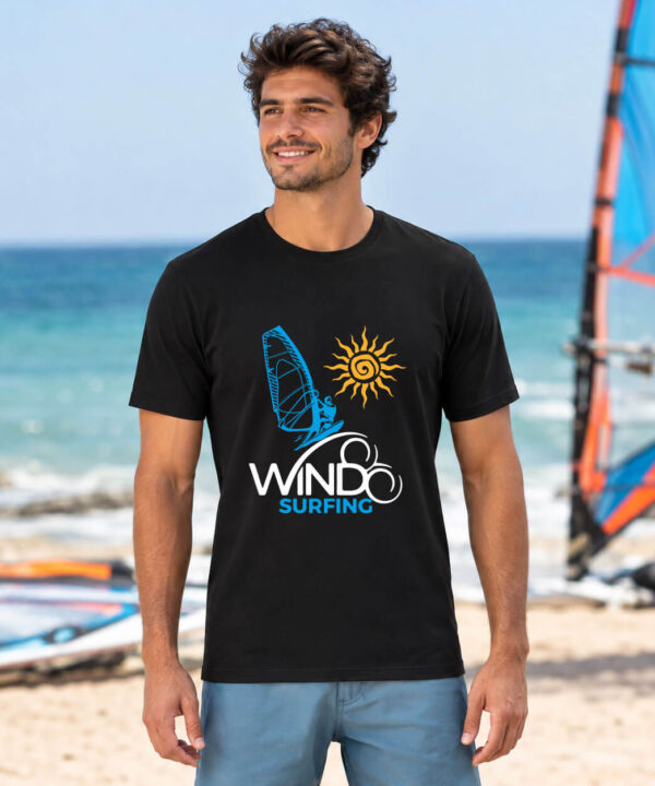 Man wearing the black Seasportees windsurfing t-shirt standing on a sunny beach with windsurfing gear in the background.